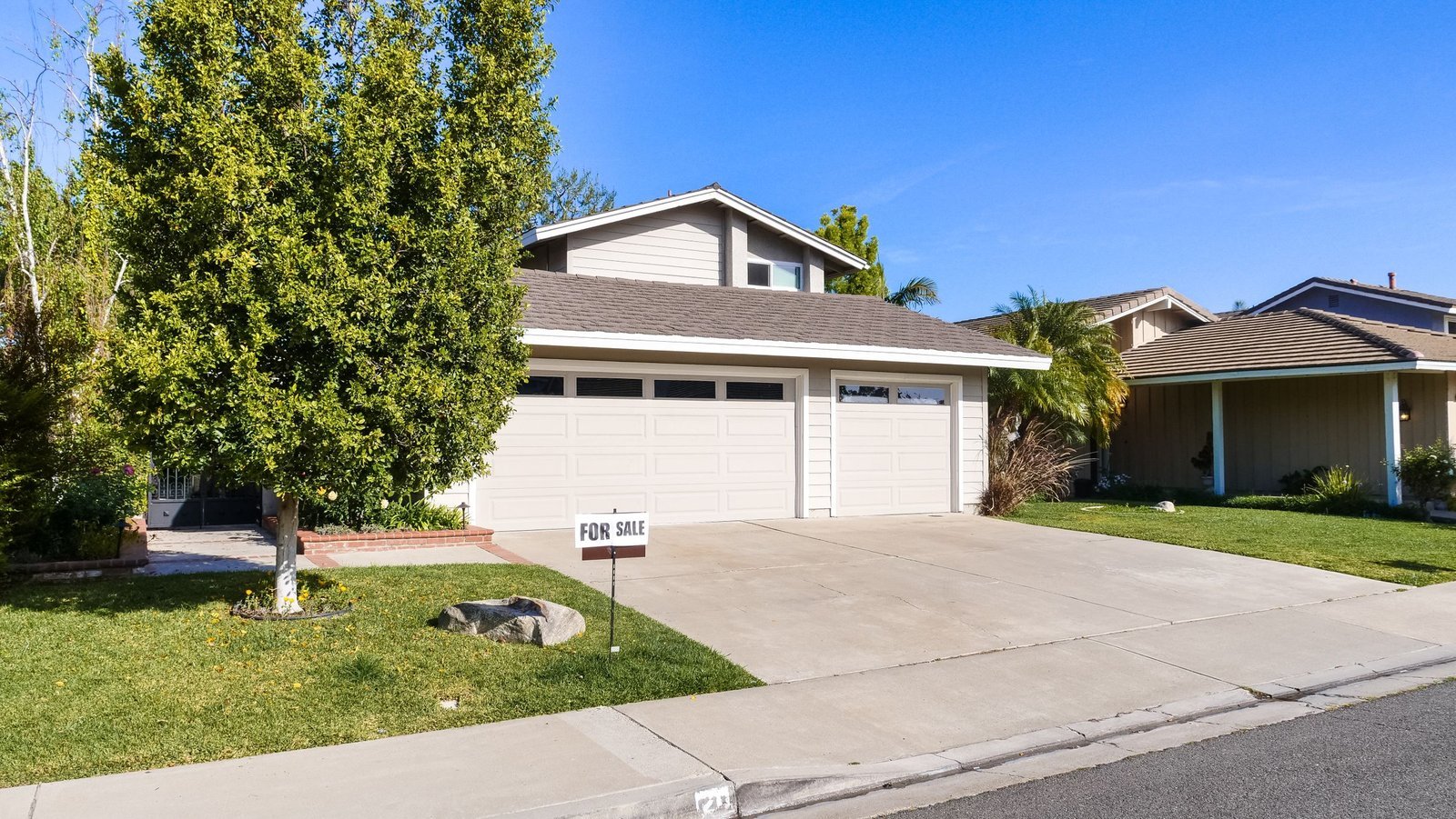 A two-story Southern California home with a For Sale sign in the front yard