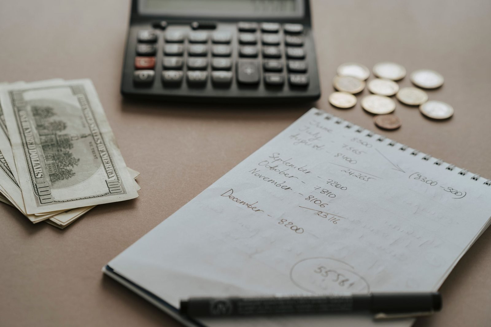 A handwritten monthly savings tally next to a calculator, cash, and coins
